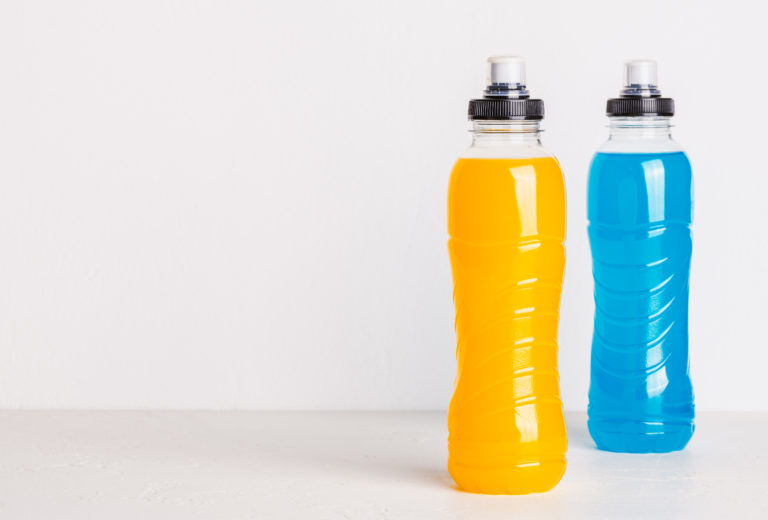 Two nonalcoholic drinks sit on a white surface. The left bottle, filled with orange liquid, and the right one, containing blue liquid, both sport black caps with pull-top spouts. These alcohol-free drinks stand against a plain white background.