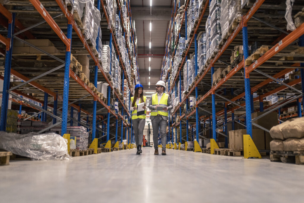 workers with hardhats reflective jackets walking through big warehouse aisle checking goods condition
