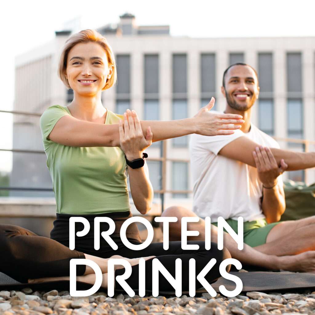Two adults sitting outdoors on yoga mats, stretching their arms and smiling. Modern building in the background. The text "PROTEIN DRINKS" is displayed at the bottom of the image.