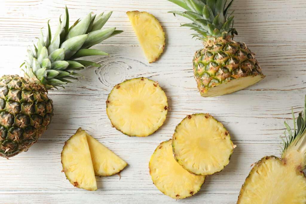 FLAVOUR OF THE YEAR 2026: PINEAPPLE 12 Two whole pineapples and several pineapple slices are arranged on a white wooden surface, showcasing the fresh, tropical look of the flavour of the year, with slices and wedges scattered artfully around.
