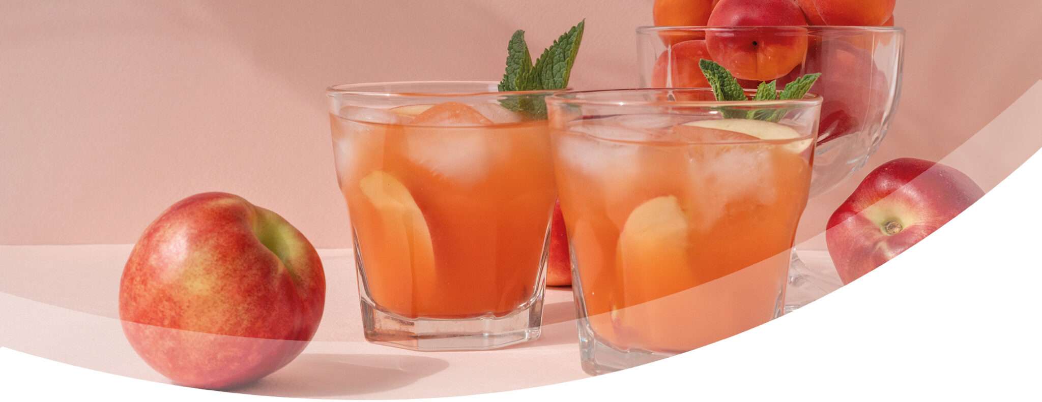 Three glasses of peach colored non alcoholic drinks with apple slices and mint, surrounded by fresh apples and a glass bowl of peaches, set against a light pink background.