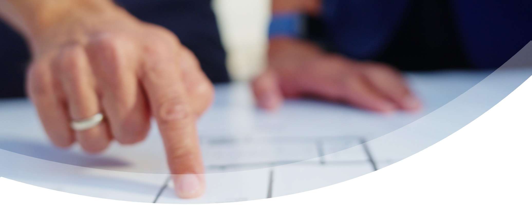 A close-up of a hand pointing to a blueprint or architectural plan on a table, with another hand resting nearby, suggesting planning or design work.
