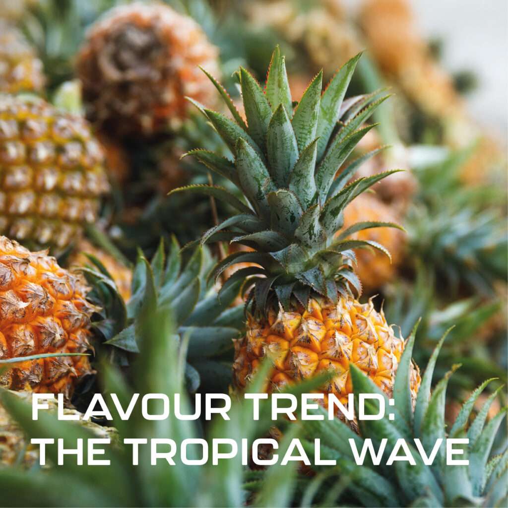 A close up of several fresh pineapples with green spiky leaves. White text over the image reads: "FLAVOUR TREND: THE TROPICAL WAVE.