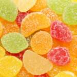 A close up view of assorted fruit flavoured gumdrops in yellow, green, orange, and red colors, all covered with a coating of sugar crystals.