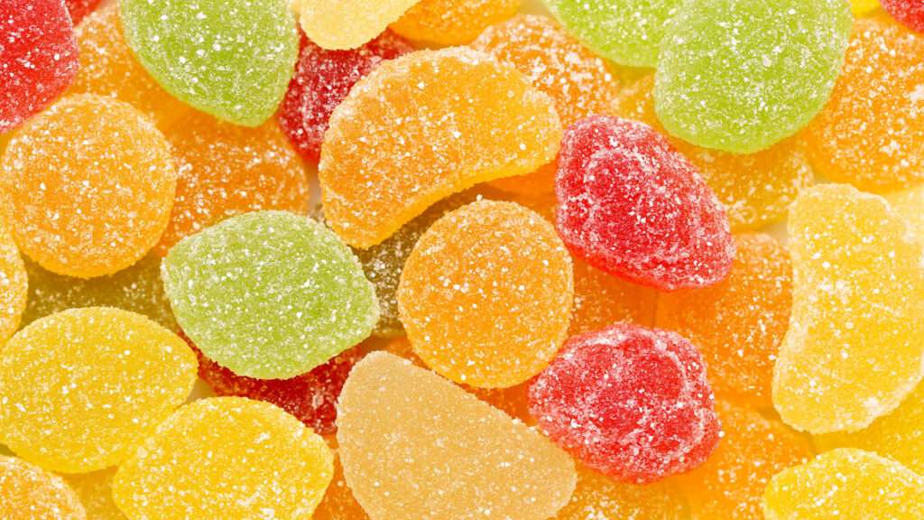 An assortment of colorful, sugar coated gummy candies in red, yellow, orange, and green, shaped like fruit slices and bursting with fruity flavour, arranged in a close up view.