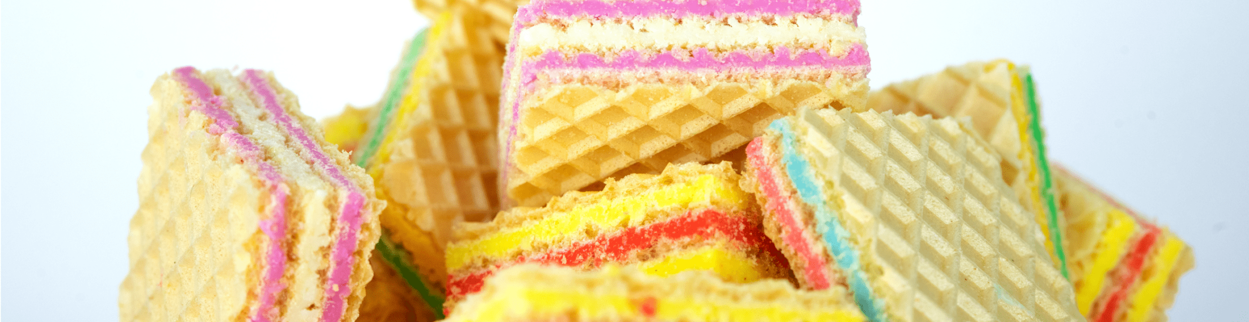 A pile of colorful wafer biscuits, with layers of pink, yellow, and blue cream between crispy, textured wafers, is displayed against a plain white background—a vibrant showcase perfect for Confectionery News or FiE highlights.